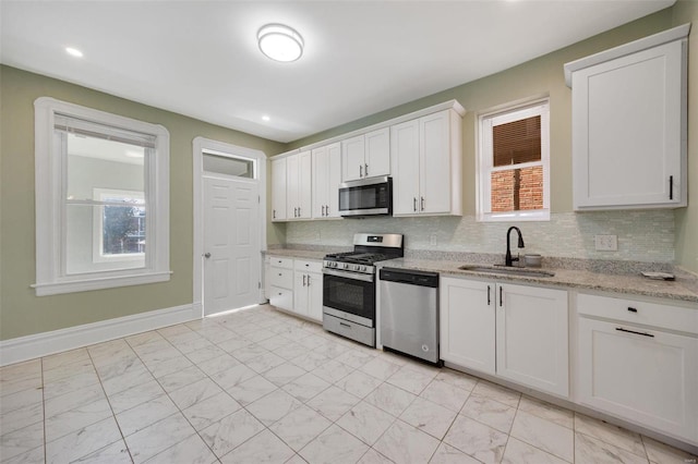 kitchen with appliances with stainless steel finishes, sink, white cabinets, decorative backsplash, and light stone counters