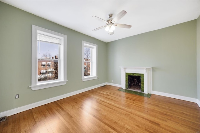 unfurnished living room with a tiled fireplace, hardwood / wood-style floors, and ceiling fan