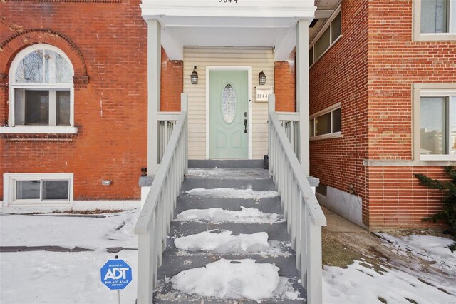 snow covered property entrance featuring brick siding