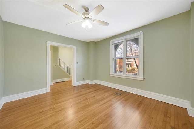 empty room featuring a ceiling fan, light wood-style flooring, baseboards, and visible vents