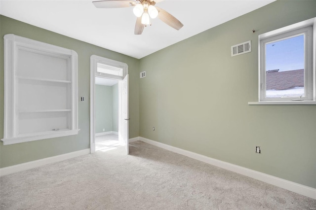 carpeted spare room featuring built in features, visible vents, baseboards, and a ceiling fan