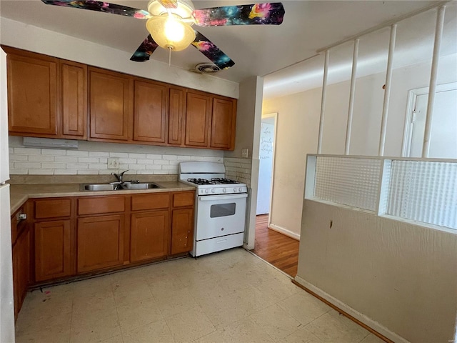 kitchen with white gas range, sink, ceiling fan, and decorative backsplash