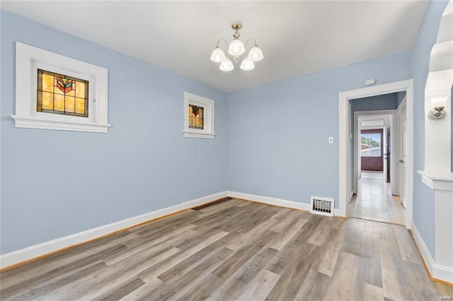 unfurnished room featuring a notable chandelier and light hardwood / wood-style flooring