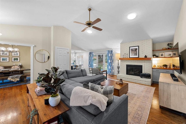 living room featuring a fireplace, dark wood-type flooring, high vaulted ceiling, and ceiling fan with notable chandelier