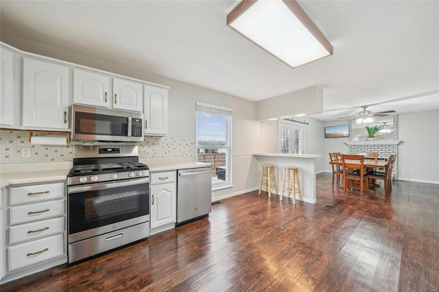 kitchen with dark hardwood / wood-style floors, white cabinets, ceiling fan, stainless steel appliances, and backsplash