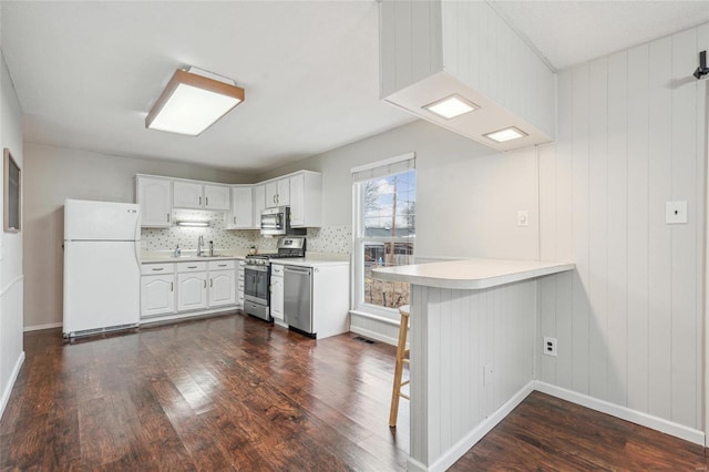 kitchen featuring appliances with stainless steel finishes, a breakfast bar, dark hardwood / wood-style floors, white cabinets, and kitchen peninsula