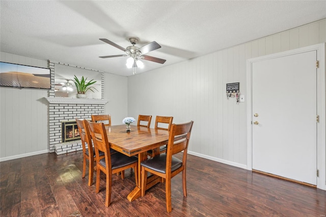 dining space with ceiling fan, a brick fireplace, a textured ceiling, and dark hardwood / wood-style flooring