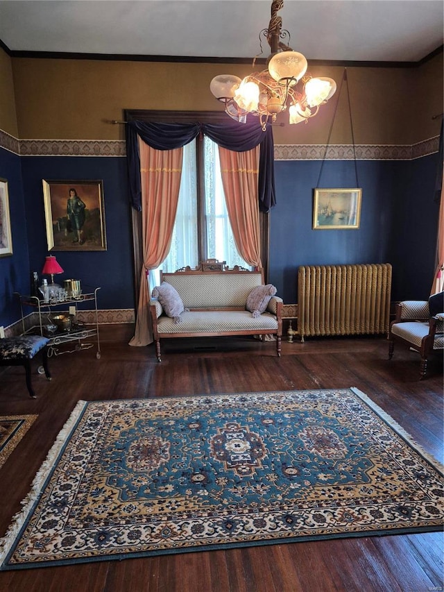 living area with wood-type flooring, ornamental molding, radiator heating unit, and an inviting chandelier