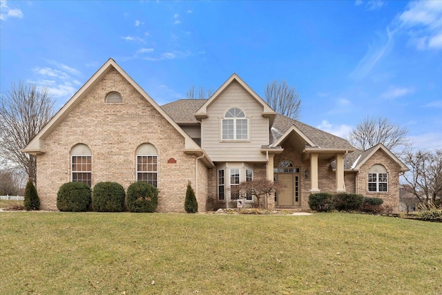 traditional-style house with a shingled roof, a front yard, and brick siding