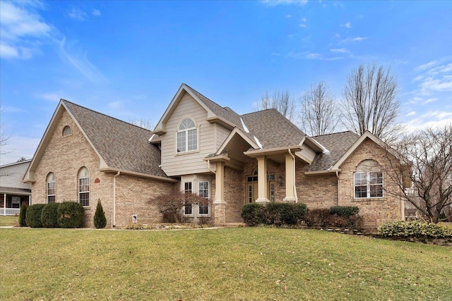 view of front of property featuring a shingled roof, a front yard, and brick siding