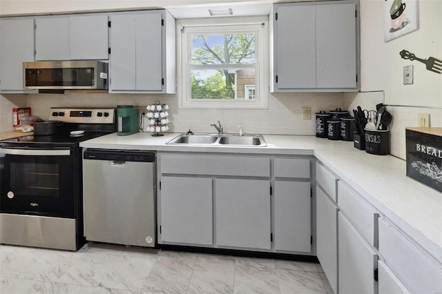 kitchen with a sink, stainless steel appliances, tasteful backsplash, marble finish floor, and light countertops