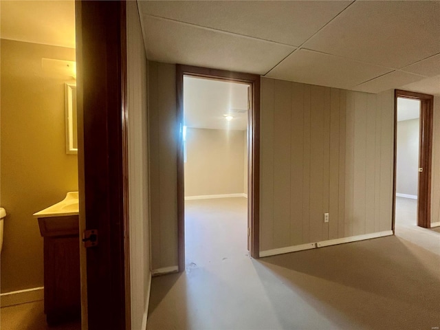 hall featuring a drop ceiling and wood walls