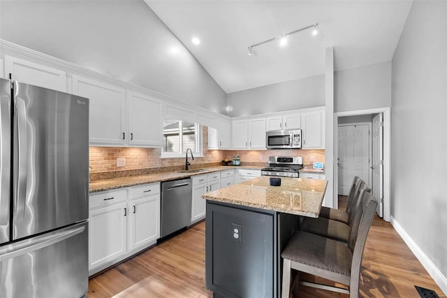 kitchen with a kitchen island, white cabinetry, sink, light stone counters, and stainless steel appliances