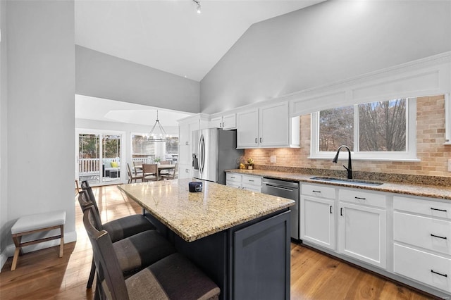 kitchen with appliances with stainless steel finishes, decorative light fixtures, white cabinetry, sink, and a center island