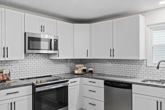 kitchen with sink, dark stone countertops, appliances with stainless steel finishes, white cabinets, and backsplash