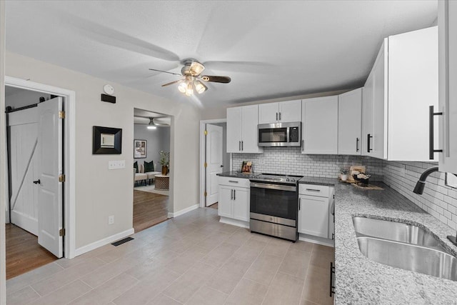 kitchen featuring sink, appliances with stainless steel finishes, white cabinetry, tasteful backsplash, and a barn door