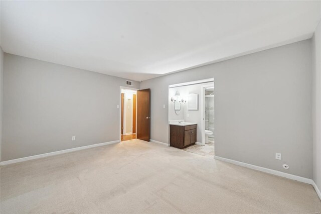 unfurnished bedroom with ensuite bathroom, sink, and light carpet