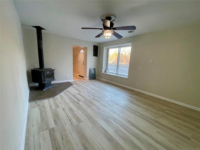 unfurnished living room with visible vents, wood finished floors, baseboards, ceiling fan, and a wood stove