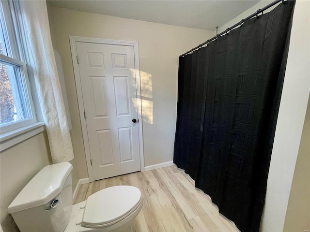 bathroom with a shower with curtain, toilet, wood finished floors, and baseboards