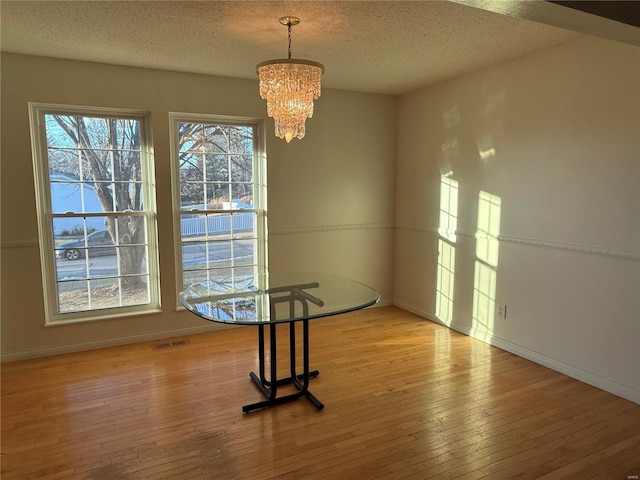 unfurnished dining area featuring light hardwood / wood-style floors, a chandelier, and a textured ceiling