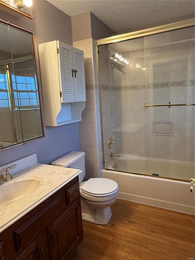 full bathroom with toilet, a textured ceiling, vanity, enclosed tub / shower combo, and hardwood / wood-style floors