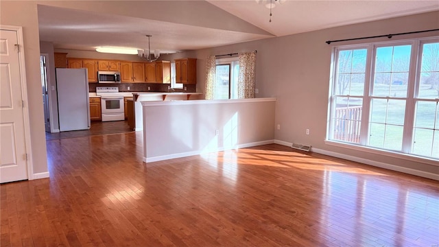 kitchen with hardwood / wood-style floors, pendant lighting, lofted ceiling, a chandelier, and white appliances