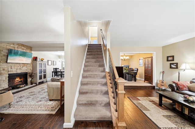 stairway with a stone fireplace, hardwood / wood-style floors, and a chandelier