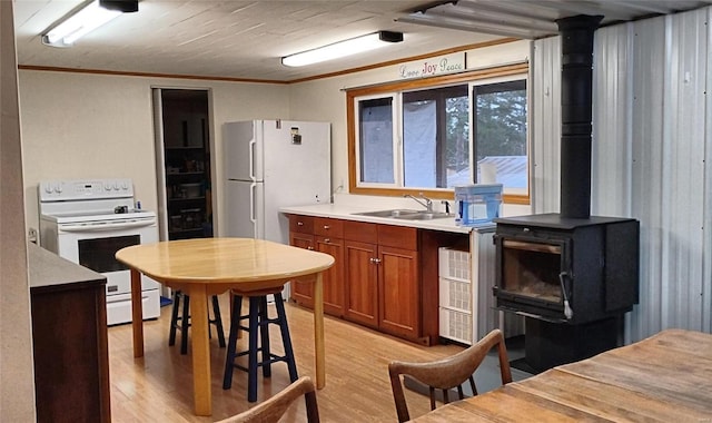 kitchen featuring sink, a wood stove, light hardwood / wood-style floors, crown molding, and white appliances