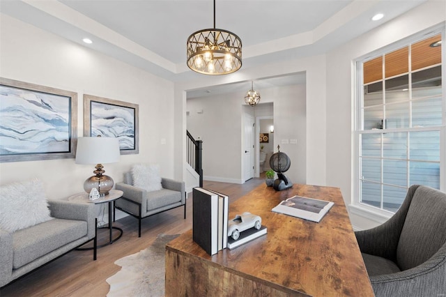 office area featuring a tray ceiling, a notable chandelier, and hardwood / wood-style flooring