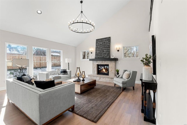 living room with high vaulted ceiling, a stone fireplace, hardwood / wood-style floors, and a notable chandelier