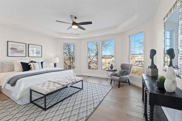 bedroom with a tray ceiling, light hardwood / wood-style floors, and ceiling fan