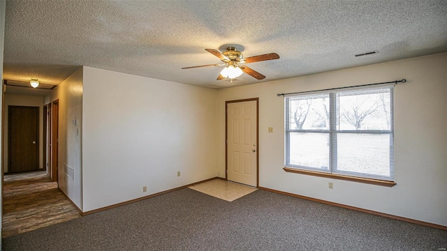 carpeted spare room with a textured ceiling, a ceiling fan, baseboards, and visible vents