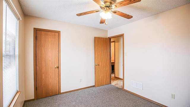 unfurnished bedroom featuring a textured ceiling, visible vents, baseboards, carpet floors, and a ceiling fan