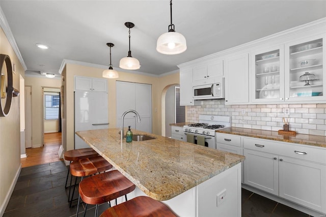 kitchen featuring a breakfast bar area, tasteful backsplash, a center island with sink, white appliances, and white cabinets