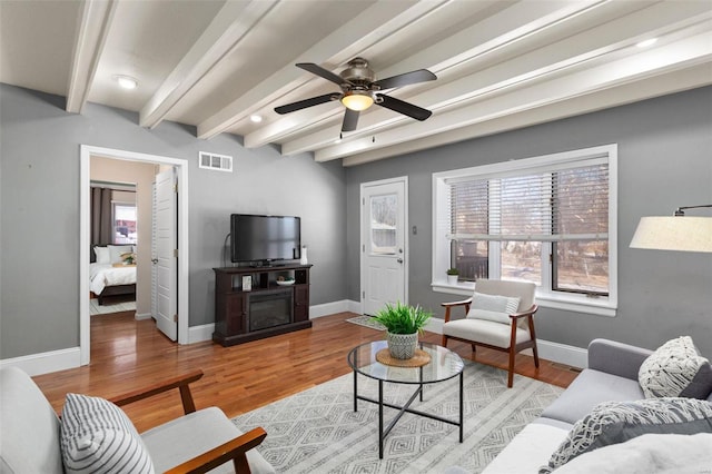 living room featuring ceiling fan, light hardwood / wood-style flooring, a fireplace, and beamed ceiling