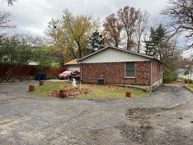 view of property exterior featuring aphalt driveway, brick siding, and fence