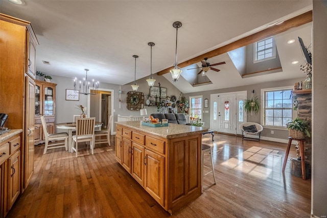 kitchen featuring pendant lighting, a breakfast bar area, light stone countertops, a kitchen island, and vaulted ceiling