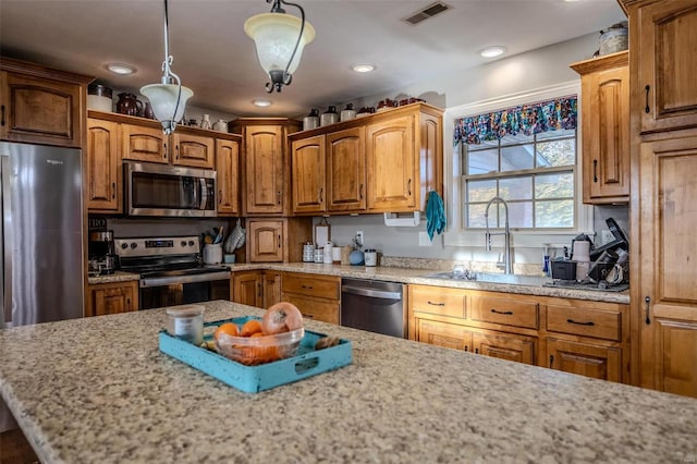 kitchen featuring stainless steel appliances, sink, pendant lighting, and light stone counters