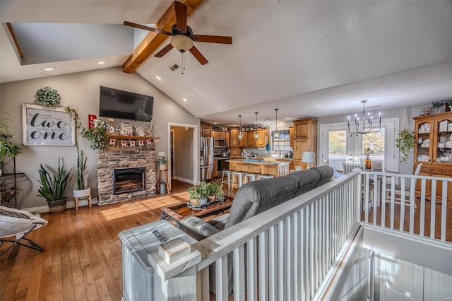 living room with vaulted ceiling with beams, ceiling fan with notable chandelier, a fireplace, and light wood-type flooring