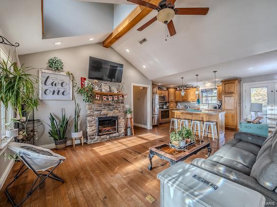 living room featuring high vaulted ceiling, light wood-type flooring, beamed ceiling, ceiling fan, and a fireplace