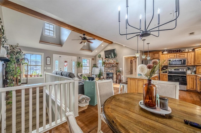 dining room with lofted ceiling with beams, light wood-type flooring, ceiling fan with notable chandelier, and a fireplace