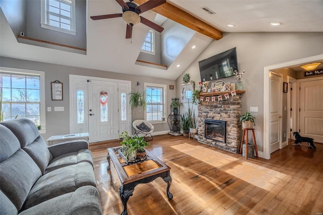 living room with a stone fireplace, high vaulted ceiling, hardwood / wood-style flooring, ceiling fan, and beam ceiling