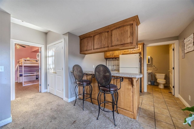 kitchen with white fridge, light carpet, and a kitchen bar