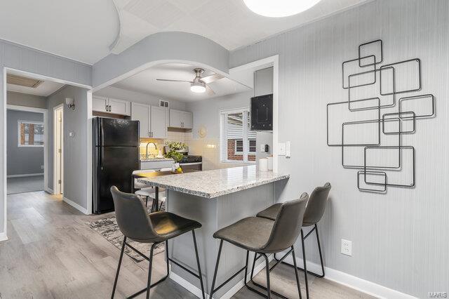 kitchen with a breakfast bar, white cabinetry, black appliances, kitchen peninsula, and light wood-type flooring