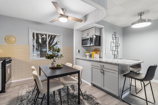 kitchen featuring gray cabinets, tile walls, light stone counters, gas range, and light wood-type flooring