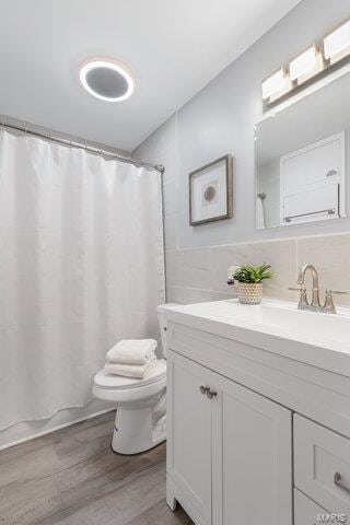 bathroom featuring toilet, wood-type flooring, tile walls, vanity, and curtained shower