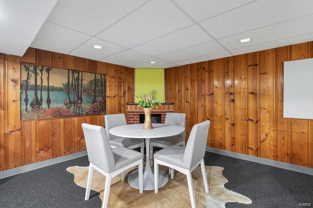 dining room featuring carpet, a drop ceiling, and wood walls