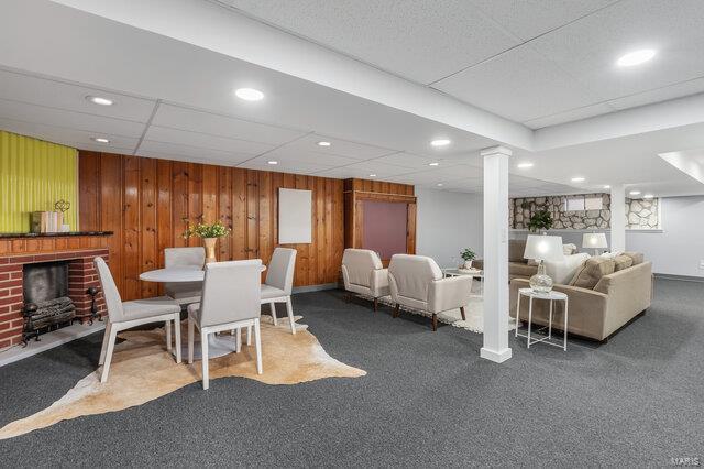 dining space with wood walls, a paneled ceiling, a fireplace, decorative columns, and carpet