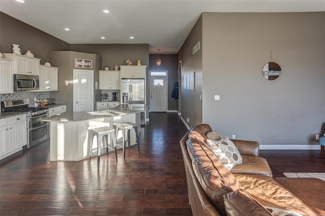 kitchen with tasteful backsplash, a kitchen breakfast bar, stainless steel appliances, light stone countertops, and a kitchen island with sink