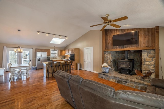 living room with lofted ceiling with skylight, ceiling fan with notable chandelier, light hardwood / wood-style flooring, and a wood stove